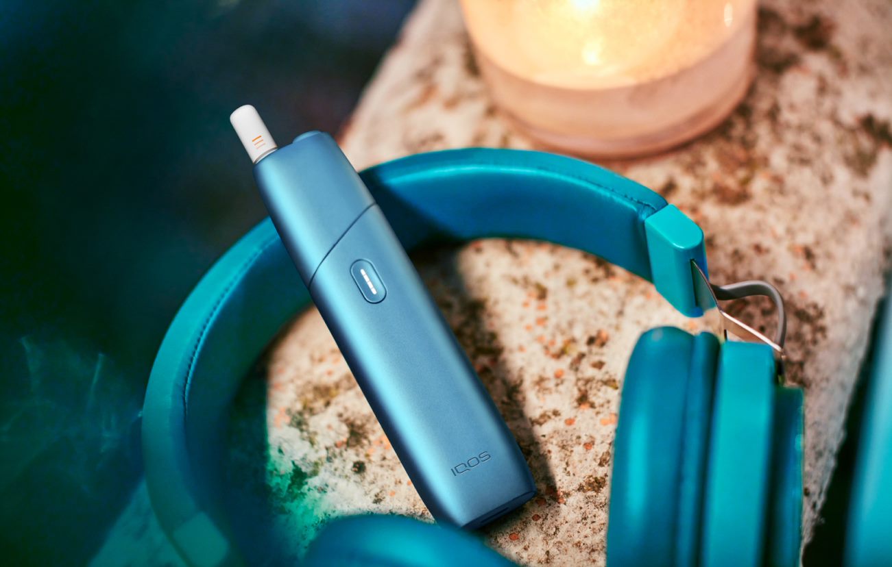 IQOS Originals One device next to turquoise headphones.